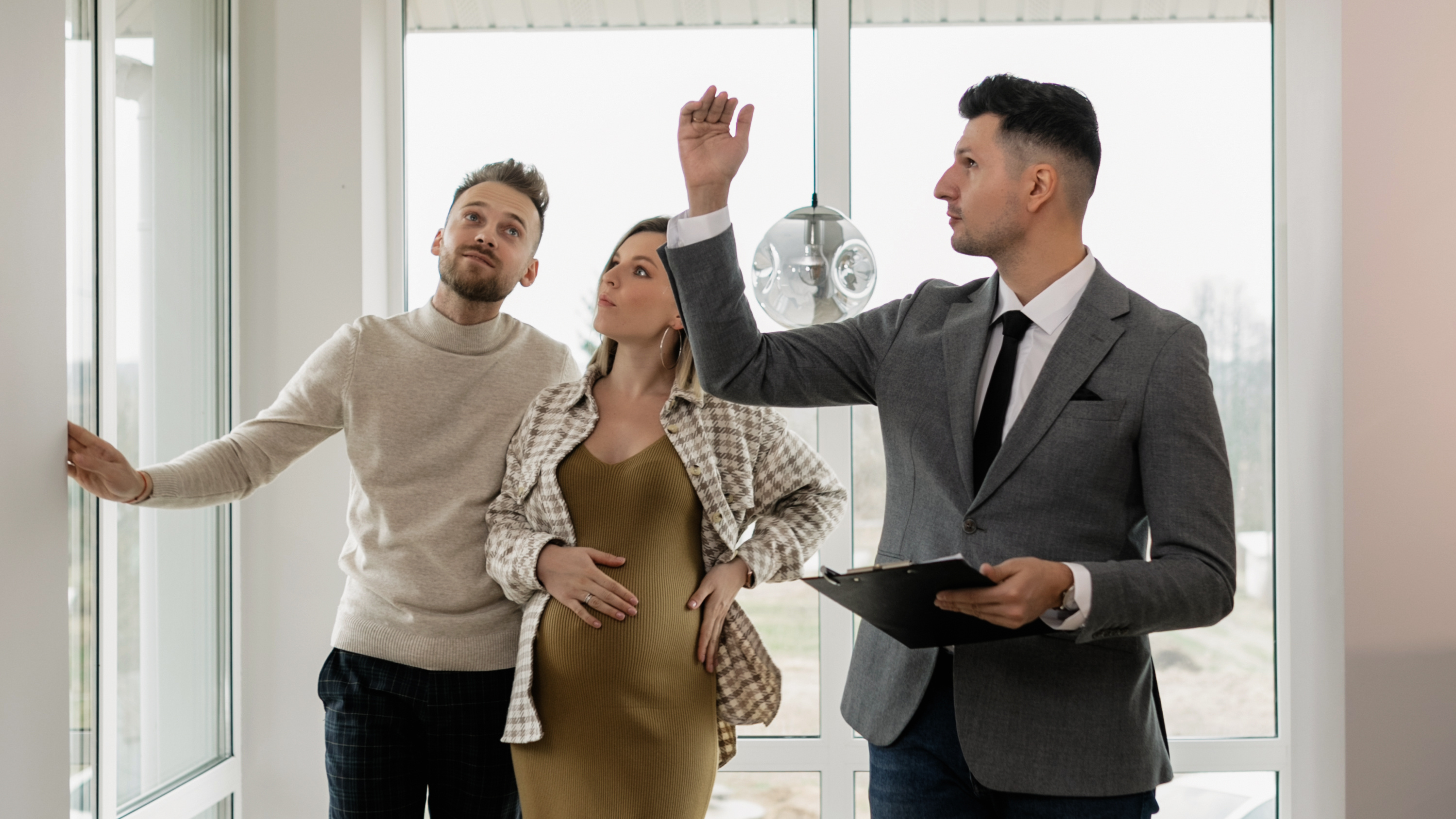 Ein Immobilienmakler der einem Paar eine Immobilie zeigt. Die Frau ist schwanger und das Haus ist für eine kleine Familie